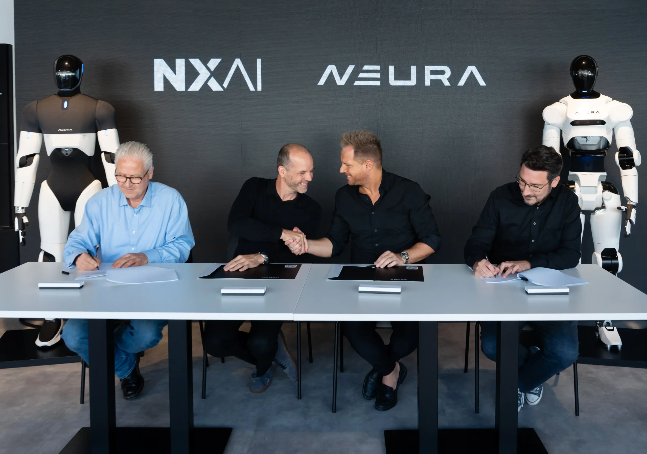 Équipes de NEURA Robotics et NXAI signant leur partenariat devant deux robots humanoïdes